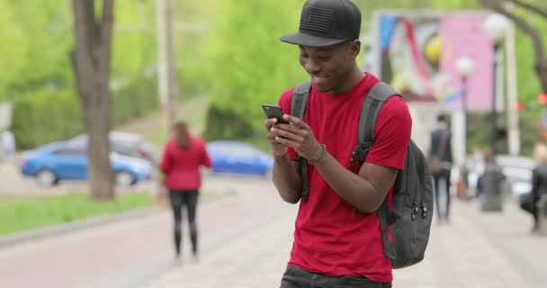 Africano americano homem em vermelho t-shirt rir usando aplicativo no telefone inteligente — Vídeo de Stock