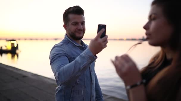 Fotografía móvil, hombre hacer fotos para la mujer en el terraplén de la ciudad — Vídeos de Stock