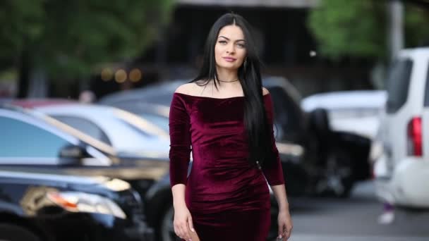Beautiful attractive brunette woman in burgundy dress walking through city — Stock Video
