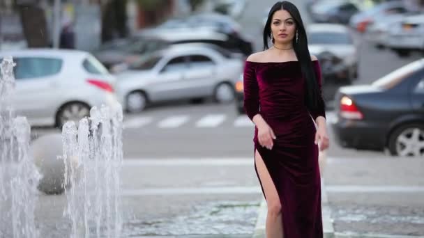 Luxury beautiful woman in burgundy summer dress walking at fountain — Stock Video