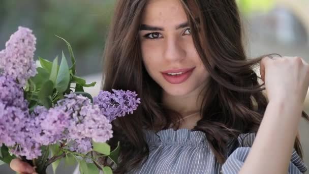 Молодая красивая женщина улыбается, держа сиреневые цветы — стоковое видео