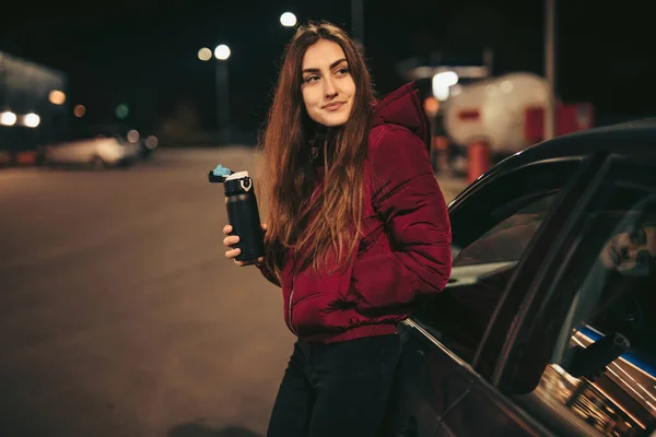 Retrato de mulher motorista com garrafa térmica no posto de gasolina, noite — Fotografia de Stock