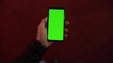 Birinci şahıs görüntüsü, alışveriş merkezinde yeşil ekranlı akıllı telefon taşıyan bir erkek.