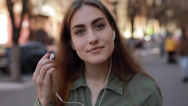 Европейка снимает наушники после прослушивания музыки в городе — стоковое видео