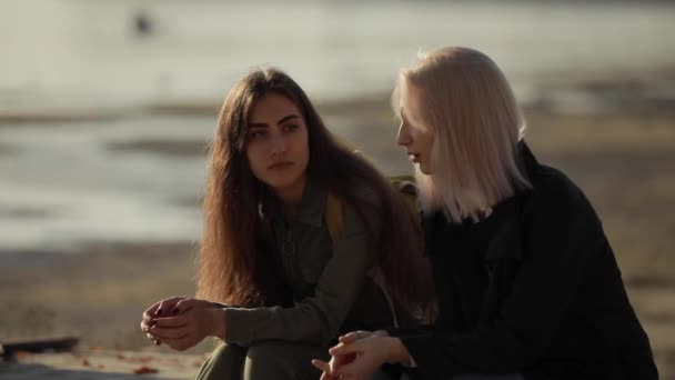 Två kvinnliga vänner sitter nära floden och pratar tillsammans — Stockvideo