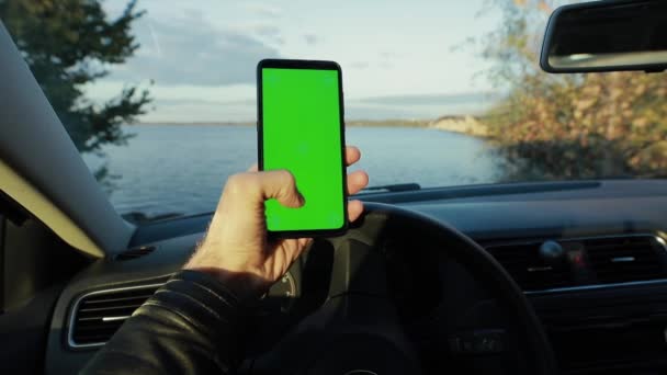 Pov, mannelijke hand holding smartphone met groen scherm in een auto bij de rivier — Stockvideo