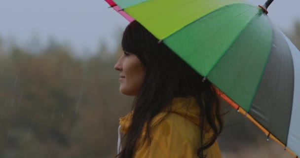 Женщина, стоящая под зонтиком, наслаждается осенним дождем — стоковое видео