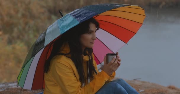 Mulher sentada sob guarda-chuva desfrutar de chuva de outono e beber chá — Vídeo de Stock