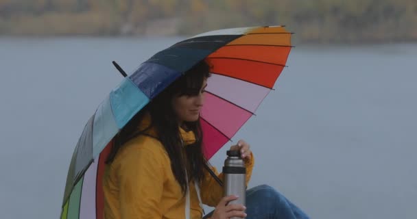 Mulher sentada sob guarda-chuva desfrutar de chuva de outono e beber chá — Vídeo de Stock