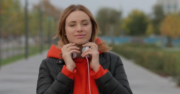 Mujer europea se pone auriculares caminando en el callejón de la ciudad — Vídeo de stock