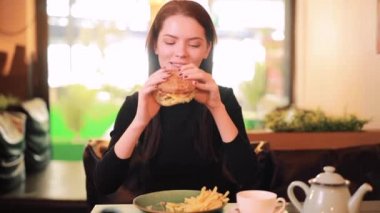 Kadın kafede hamburger yiyor.