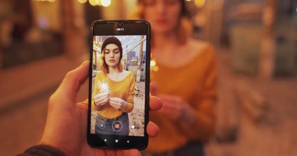 Ung kvinna med tomtebloss firar nyår i staden, fotografering på smartphone — Stockvideo