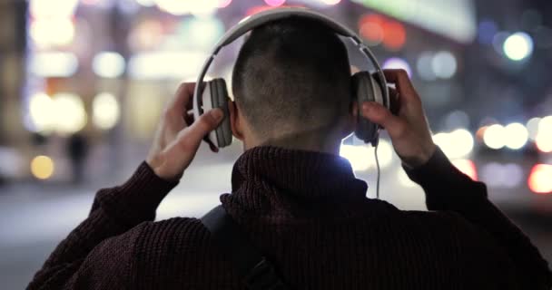 Achteraanzicht man draagt koptelefoon in de nacht stad — Stockvideo