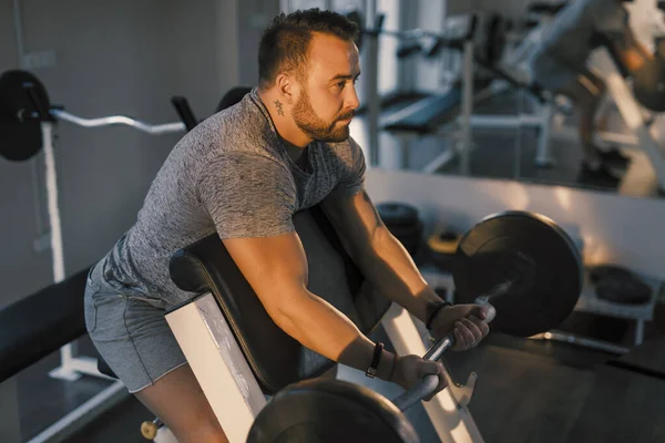 Hombre levantando la barra en un gimnasio en EZ barra predicador rizo, ejercicio bíceps — Foto de Stock