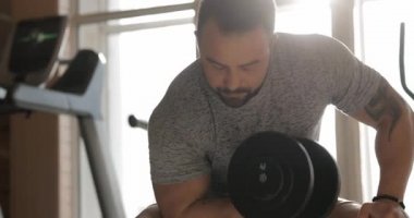 Salonda dambılları kaldıran bir adam kol kasları için egzersiz yapıyor.