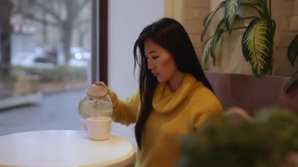 Азиатка пьет чай сидя в кафе — стоковое видео