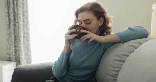 Hezká mladá žena sedí na útulné pohovce a pije čaj — Stock video