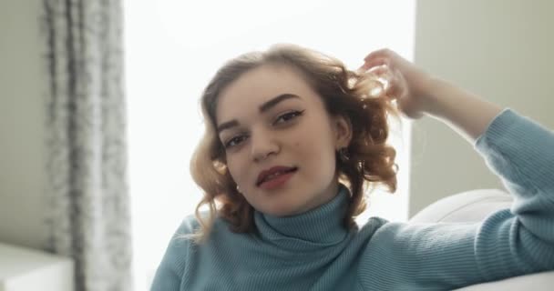 Mooie jonge kokette vrouw zit op een gezellige bank flirten met mij — Stockvideo