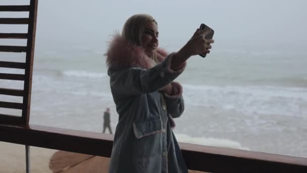 Egy nő szelfit készít mobiltelefonnal a tenger közelében, lassított mozgás — Stock videók