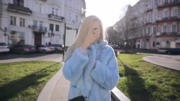 Блондинка гуляет по городу в холодный солнечный день — стоковое видео