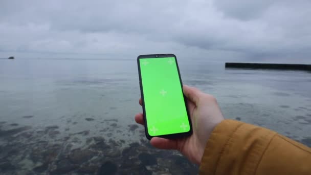 Mano masculina sosteniendo la pantalla verde en blanco del teléfono inteligente cerca del mar — Vídeo de stock