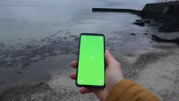Мужская рука держит чистый зеленый экран смартфона у моря — стоковое видео