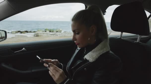 Žena cestující pomocí smartphone sedí v autě s výhledem na moře — Stock video