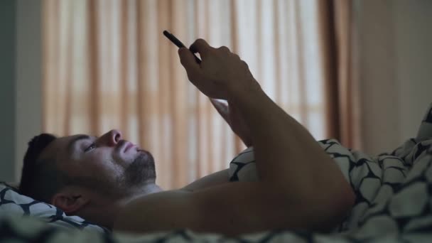 Hombre usando teléfono móvil acostado en una cama — Vídeos de Stock