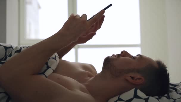 Egy férfi, aki mobiltelefont hord az ágyban. — Stock videók