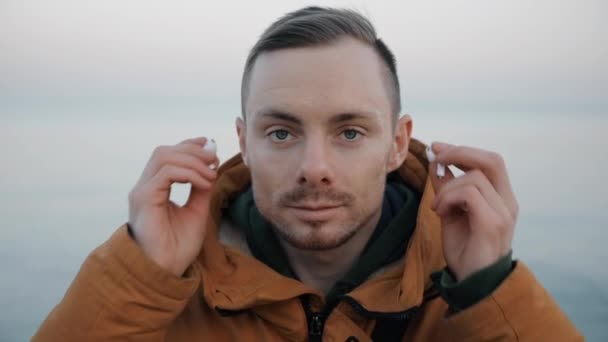 Schöner selbstbewusster Mann setzt sich am Strand Kopfhörer auf — Stockvideo