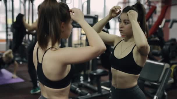 Mujer joven y bonita de pie ante el espejo y posando en un gimnasio — Vídeos de Stock