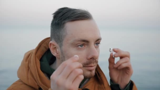 Przystojny, pewny siebie mężczyzna zakłada słuchawki na plaży morskiej. — Wideo stockowe