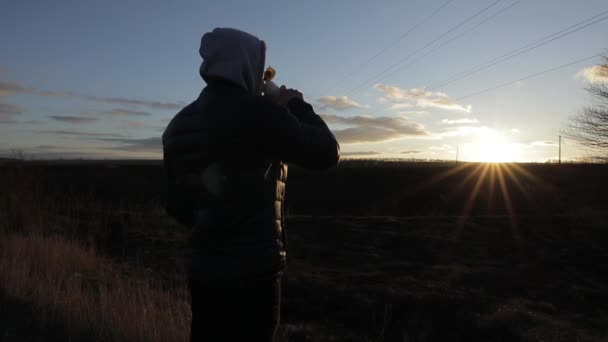Silhouet van de mens die warme thee drinkt uit de thermoskan bij zonsondergang — Stockvideo