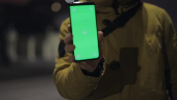 Hombre mostrando la pantalla verde vacía del teléfono inteligente por la noche — Vídeos de Stock