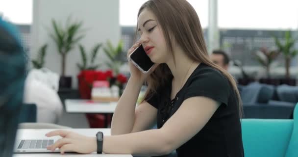 Zajęta kobieta siedzi w kawiarni i rozmawia przez telefon. — Wideo stockowe