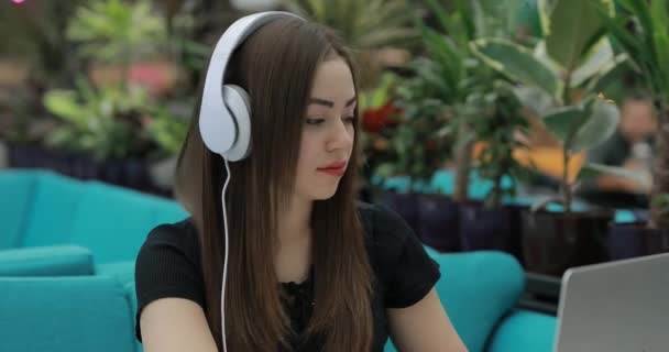 Mujer blogger sentada y trabajando en cafetería escuchando música en auriculares — Vídeo de stock