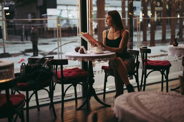 Ung kvinna läser bok på café — Stockfoto