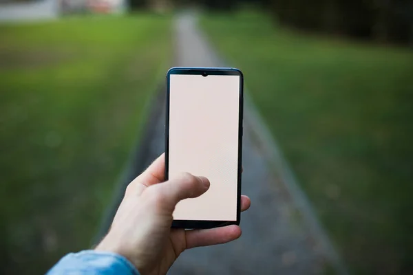 Hand holding smartphone with blank display on alley — Stockfoto