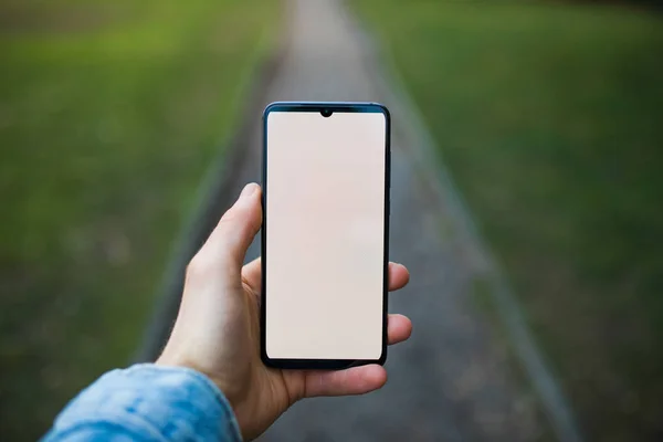 Mockup of hand holding smartphone with blank display on alley — 图库照片