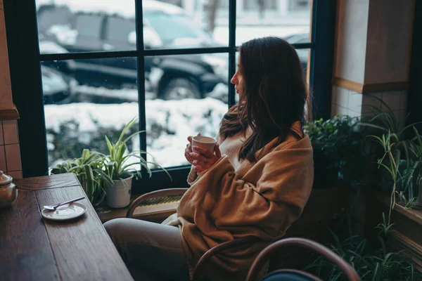 Молодая женщина пьет чай в кафе, глядя в окно — стоковое фото