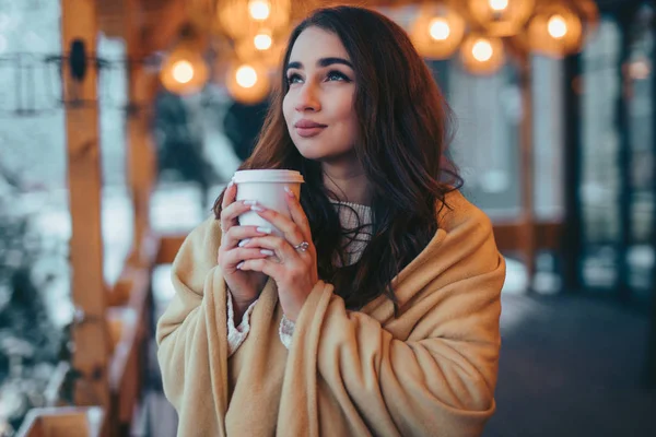 ผู้หญิงสวยถือถ้วยกาแฟกระดาษบนระเบียงคาเฟ่ในวันฤดูหนาว — ภาพถ่ายสต็อก