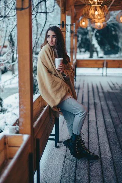 Hermosa mujer sosteniendo taza de café de papel en la terraza de la cafetería en el día de invierno —  Fotos de Stock