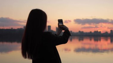 Silhouette of woman photographing cityscape sunset
