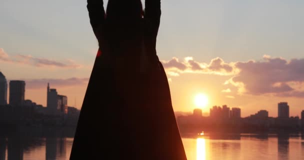 Silhueta de mulher com as mãos levantadas olhando para o nascer do sol da paisagem urbana — Vídeo de Stock