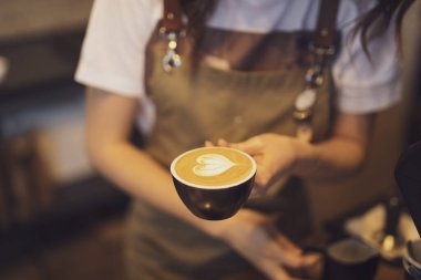 Kapalı kahve fincanı. Kadın baristanın ellerine süt dökülüyor.