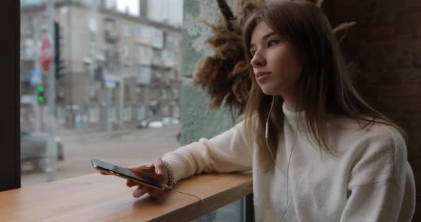Mujer joven escuchando su música favorita con auriculares en la cafetería — Vídeo de stock