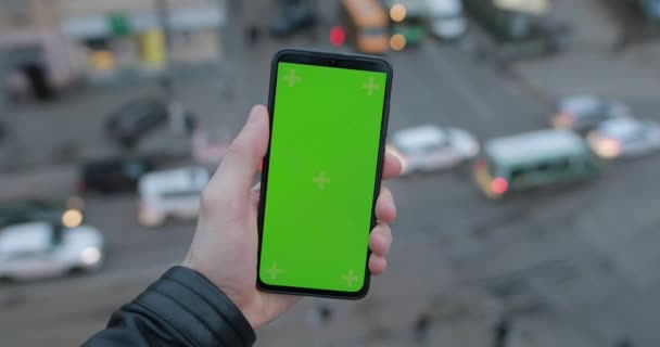Male hand holding smartphone with green screen, car traffic background — Αρχείο Βίντεο