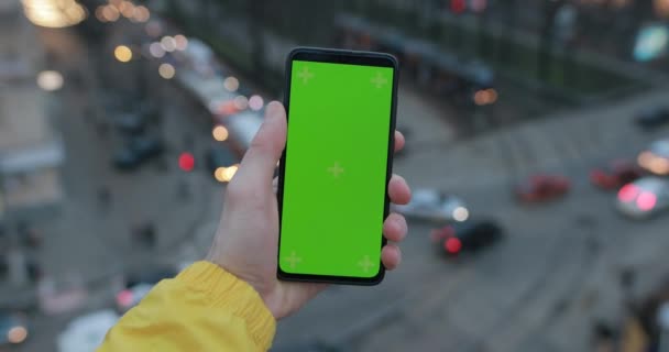 Male hand holding smartphone with green screen, car traffic background — Stockvideo