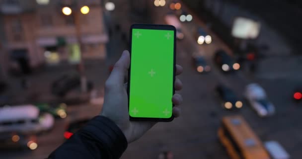 Male hand holding smartphone with green screen, car traffic background — Αρχείο Βίντεο