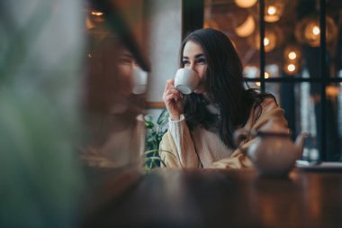 Young woman drinking tea in cafe looking through window